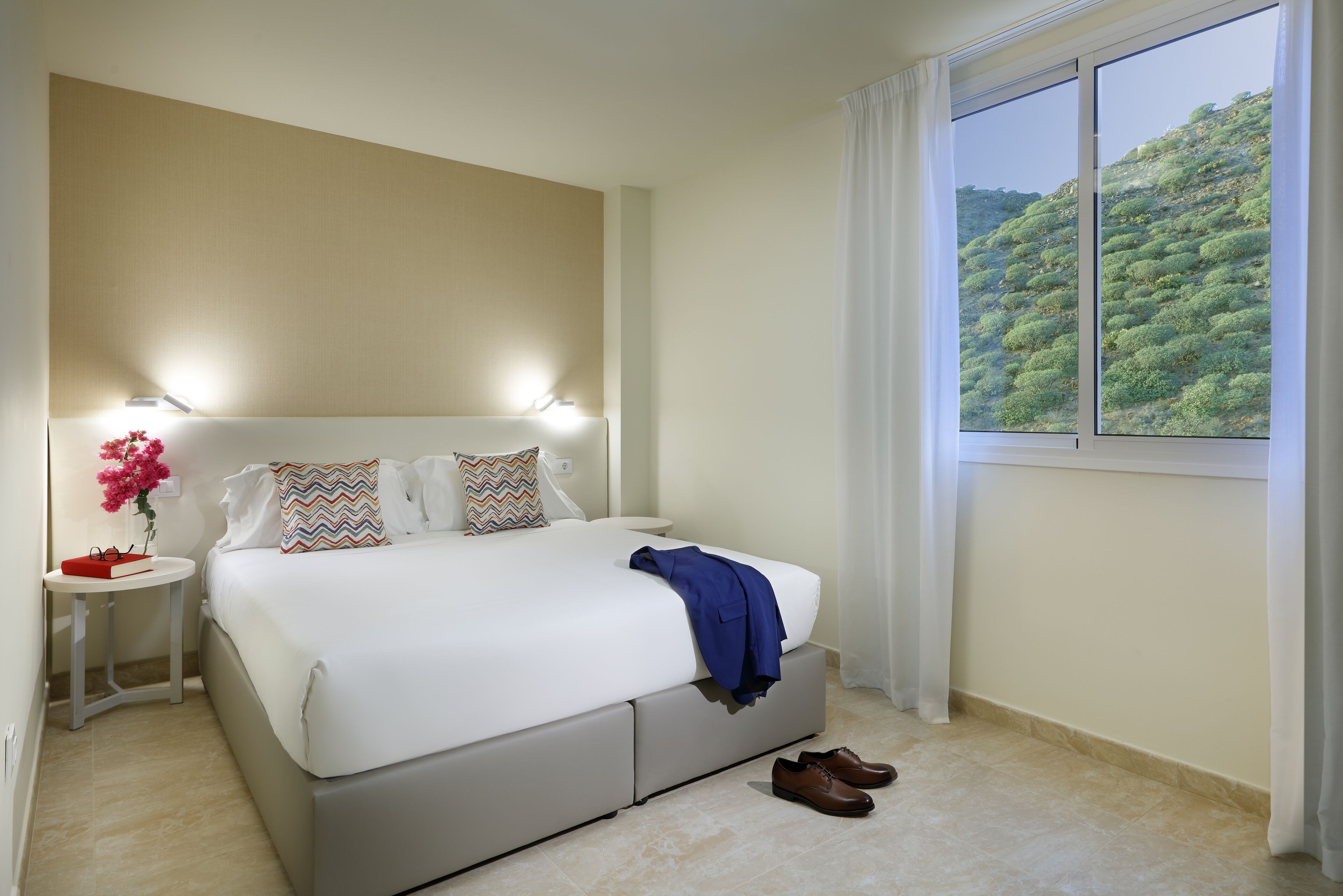 A neatly arranged bedroom with a large bed, bedside tables, and a window with a view of greenery.