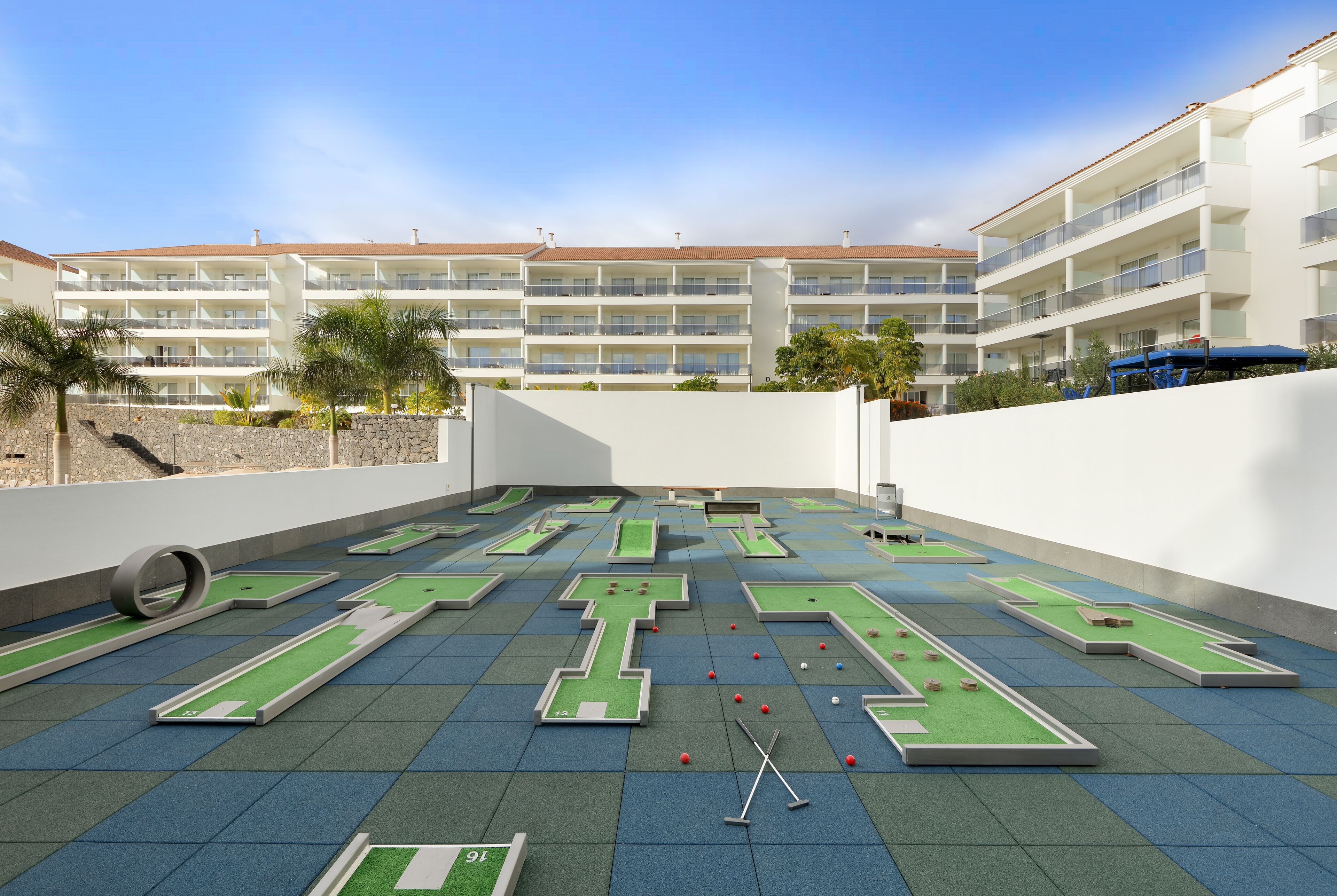 A rooftop with multiple mini-golf courses, a pool table, and a tennis court.