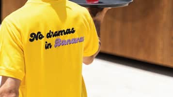 A person in a yellow shirt with "No dramas in Banana" text, holding a tray with a drink and a banana.