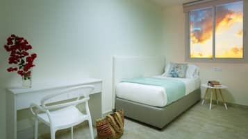 Een slaapkamer met een bed, een bureau, een stoel, een raam met uitzicht op een zonsondergang, en een kleine tafel met boeken.