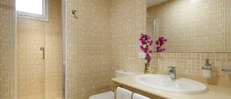 A bathroom with beige tiled walls, a white sink, a toilet, and a glass shower enclosure.