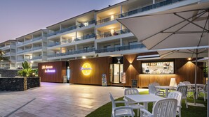 Een hotel met meerdere balkons, terraszitplaatsen en een goed verlichte ingang.