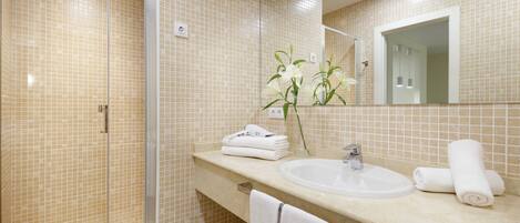 A bathroom with a glass shower enclosure, a sink, and a mirror.