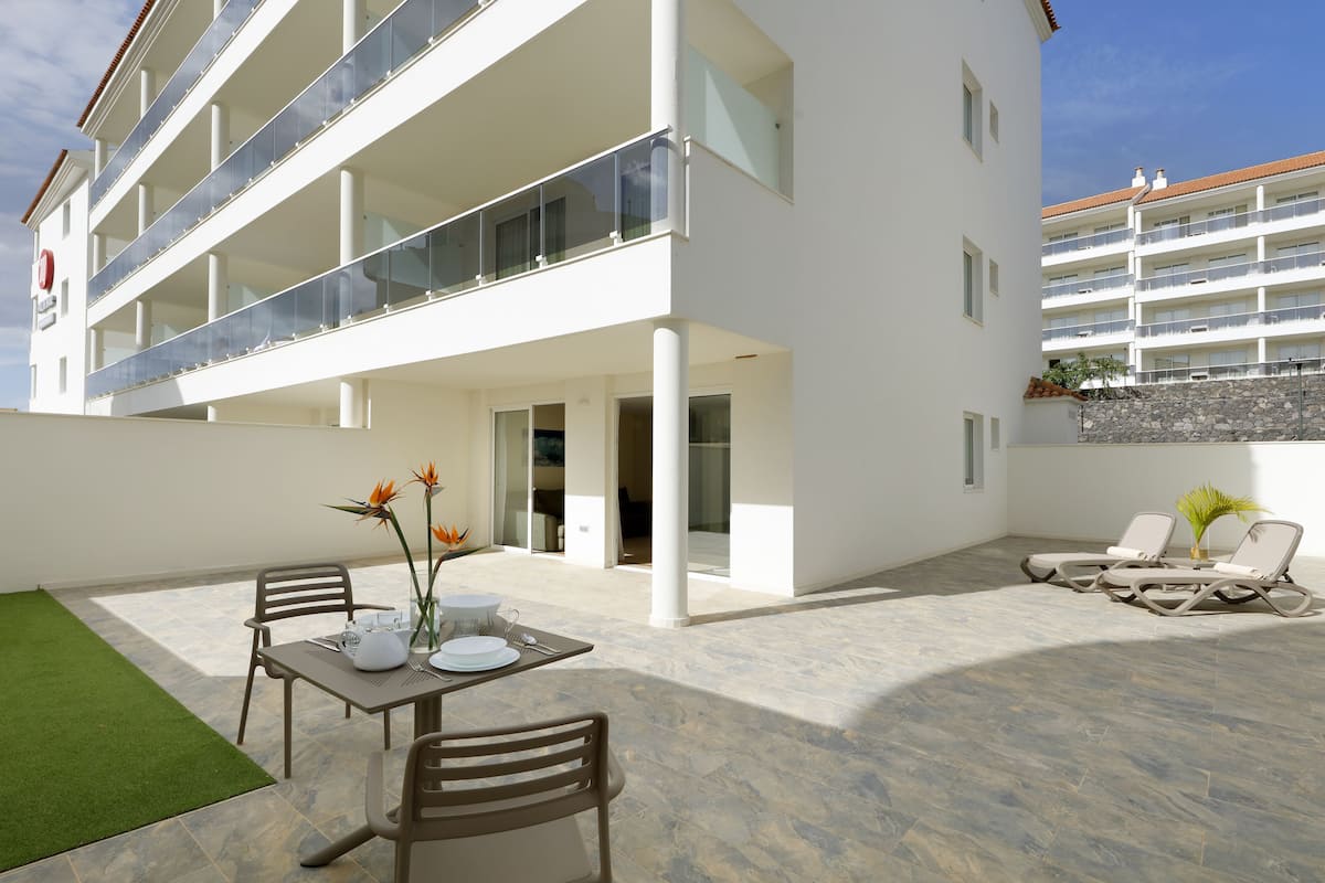Een modern gebouw met een overdekt terras, inclusief een eettafel, stoelen en lounge fauteuils.
