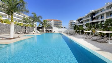 Una piscina con sillas de descanso y palmeras, rodeada de edificios modernos con balcones.