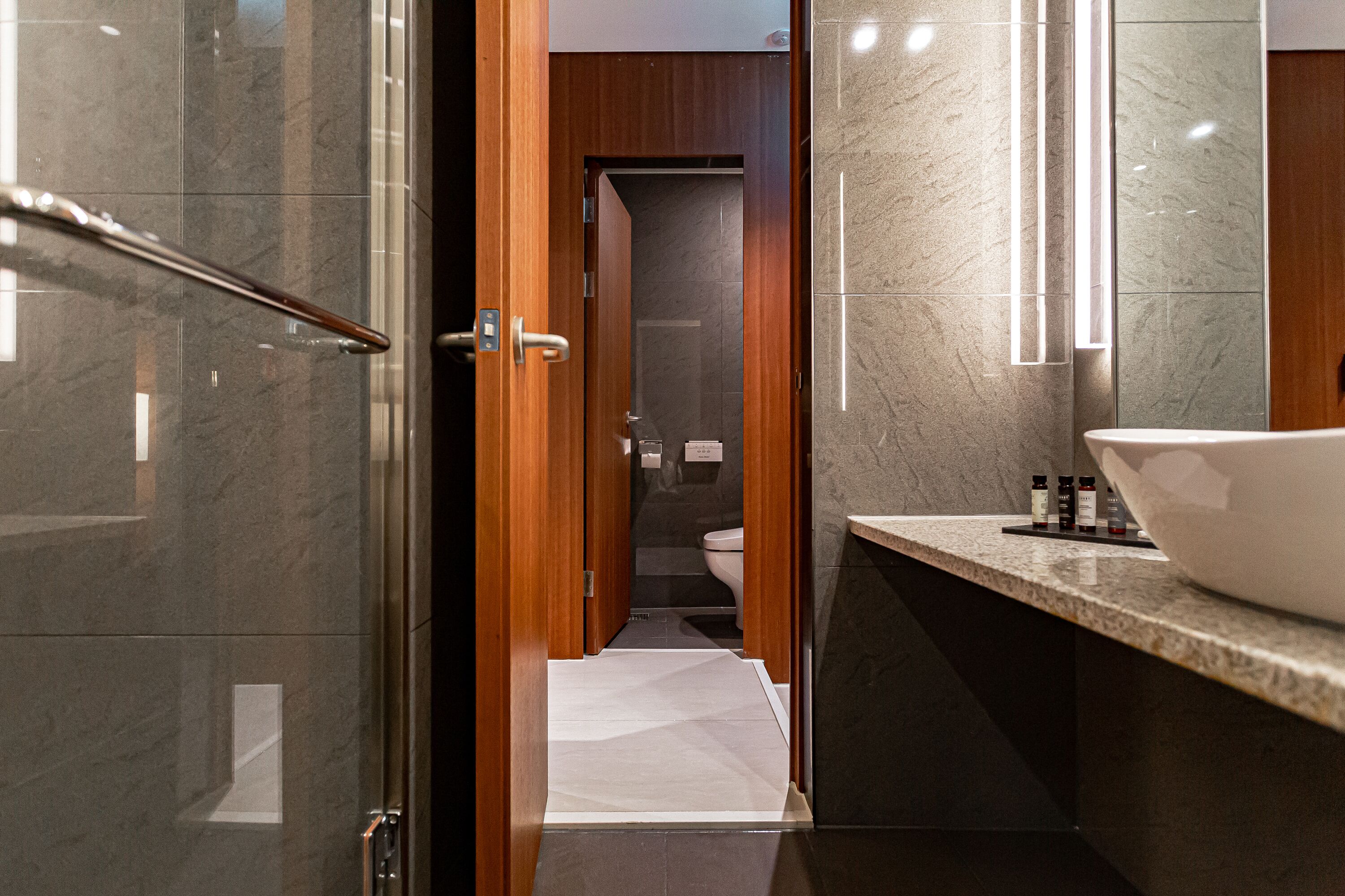 A modern bathroom with a large mirror, a wooden door, and a white sink.