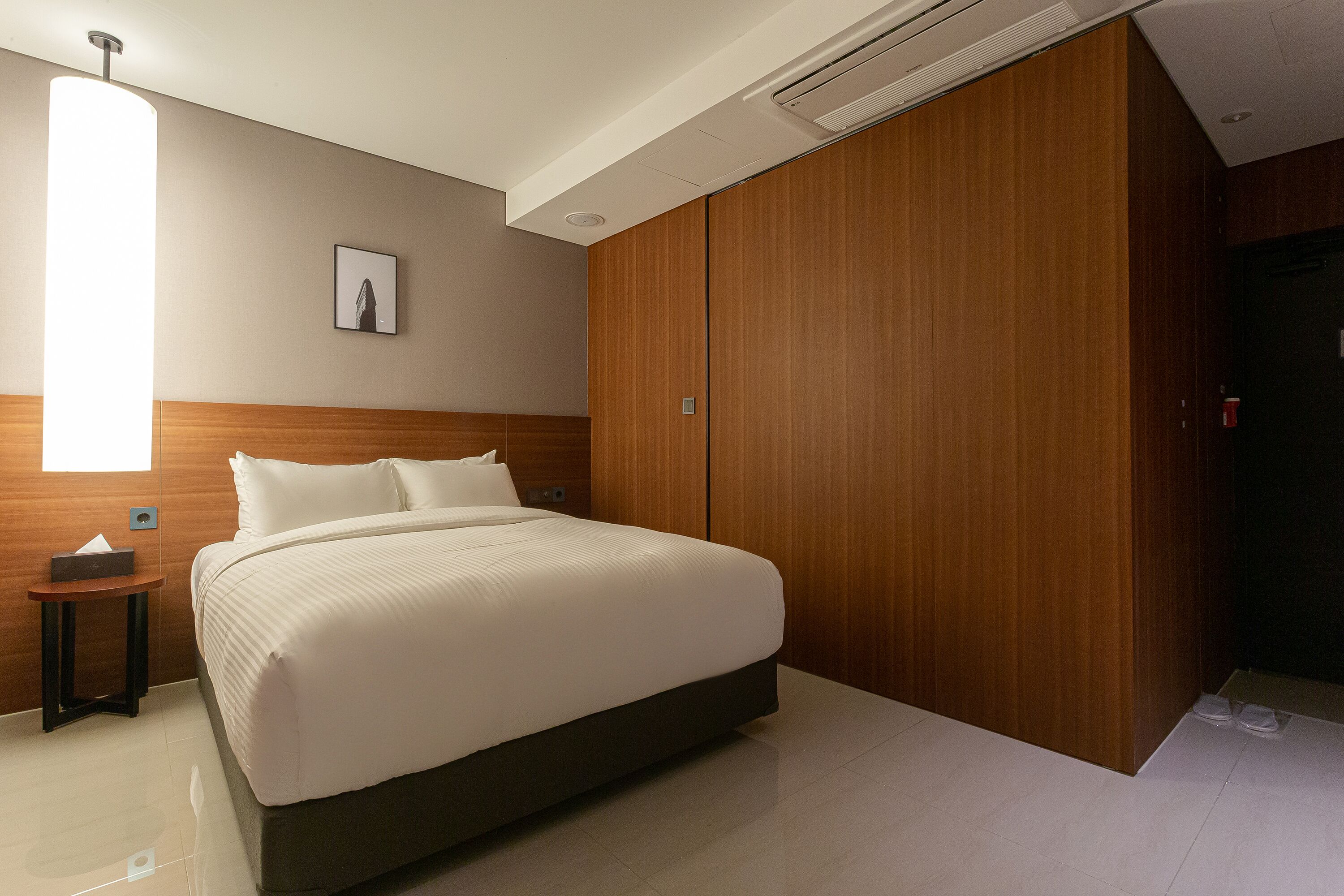 A modern hotel room with a large bed, wooden wardrobe, and a bedside table.