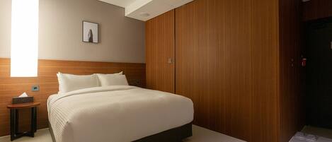 A modern hotel room with a large bed, wooden wardrobe, and a bedside table.