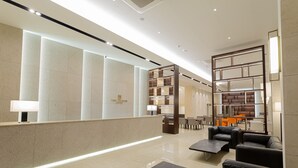 A modern hotel lobby with a reception desk, seating area, and a large mirror. - Topcloud Hotel Iksan (Iksan)