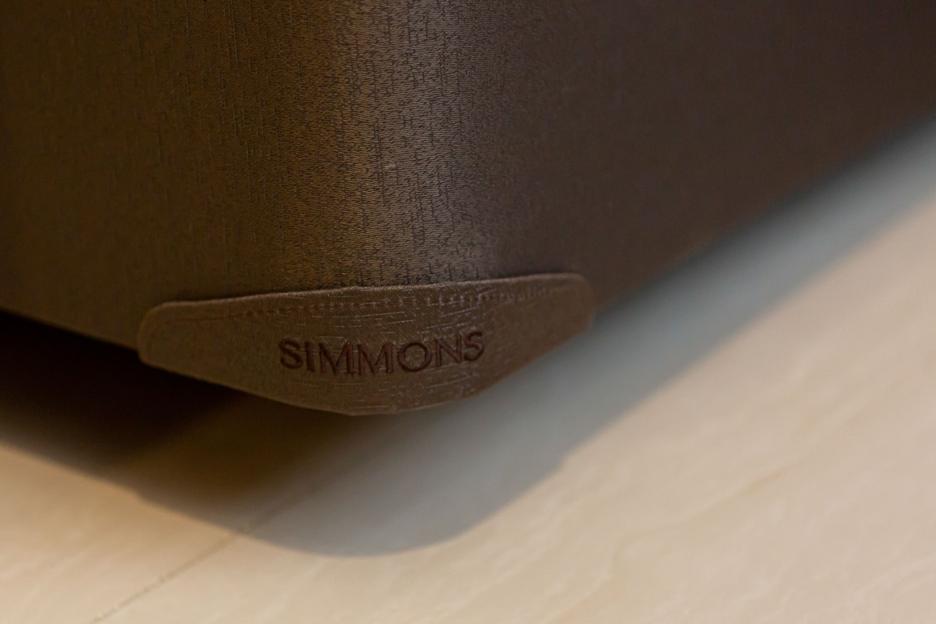 A close-up of a brown leather surface with the brand name "SIMMONS" embossed on it.