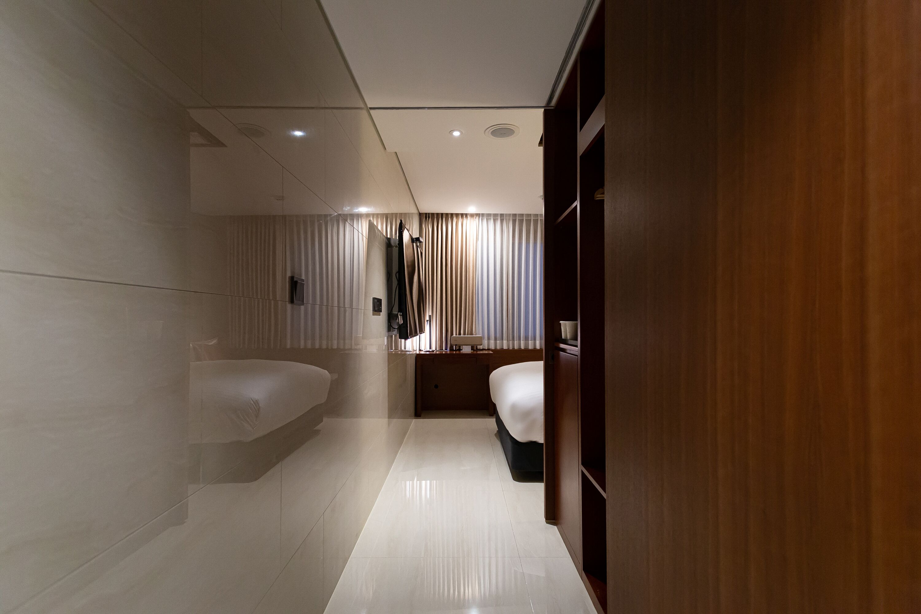 Una habitación de hotel moderna con una cama grande, otra más pequeña, un tocador con espejo y un armario de madera.
