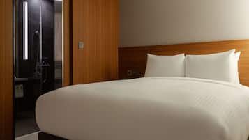 A hotel room with a large bed, wooden headboard, and a glass shower enclosure.