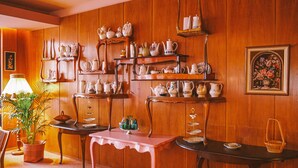 Una habitación con paneles de madera, varias estanterías que exhiben artículos de cerámica, una mesa con un vaso decorativo y un cuadro floral enmarcado.