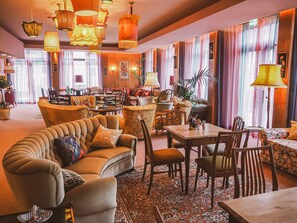 A spacious lounge area with comfortable seating, a dining area, and a view of the city. - Boutique Hotel Stadtmitte (Muelheim an der Ruhr)