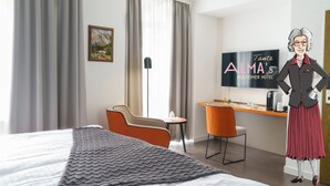 Habitación de hotel con cama, escritorio, silla anaranjada, televisor y un cuadro en la pared.