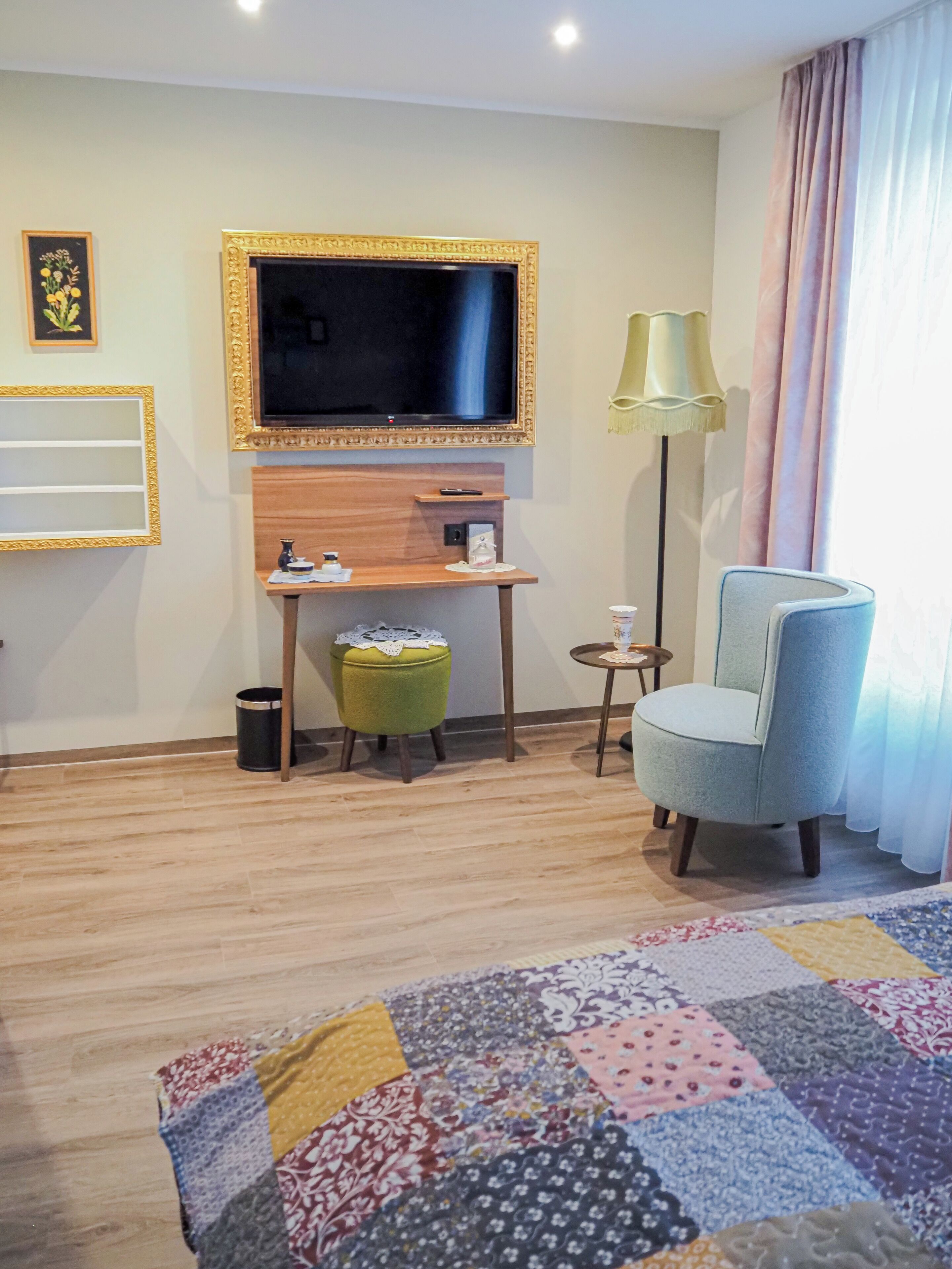 Hotelkamer met televisie, bureau, stoel, vloerlamp en een lappendeken.