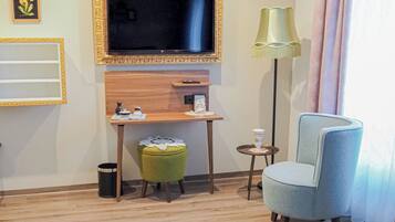 Hotelkamer met televisie, bureau, stoel, vloerlamp en een lappendeken.