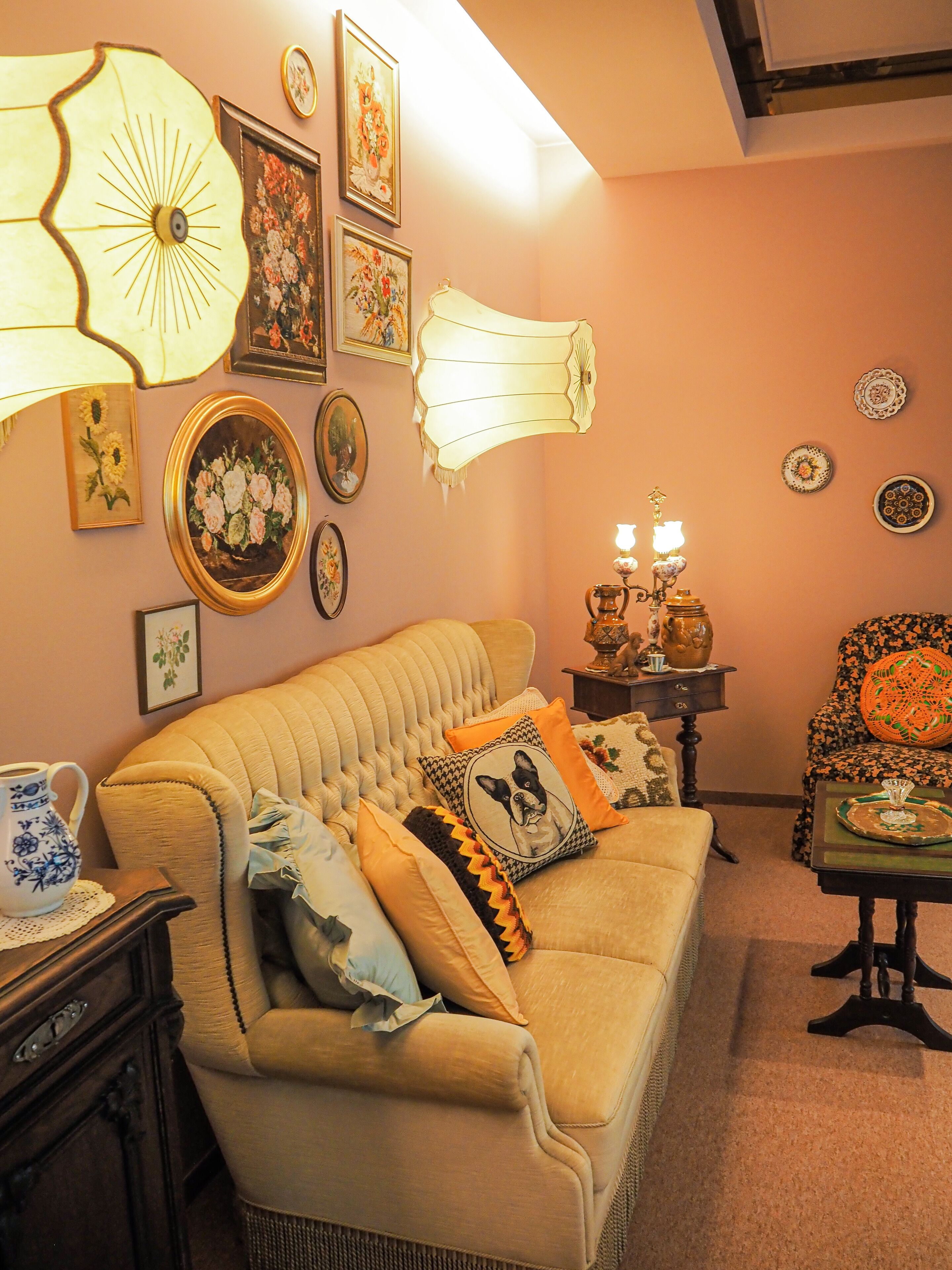 Una sala de estar acogedora con un sofá capitonado, almohadones decorativos, lámparas fijadas a la pared y cuadros con motivos florales.