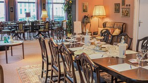 Un comedor amplio con varias mesas y sillas, un ventanal con cortinas y una zona de estar acogedora con una lámpara y un sofá.