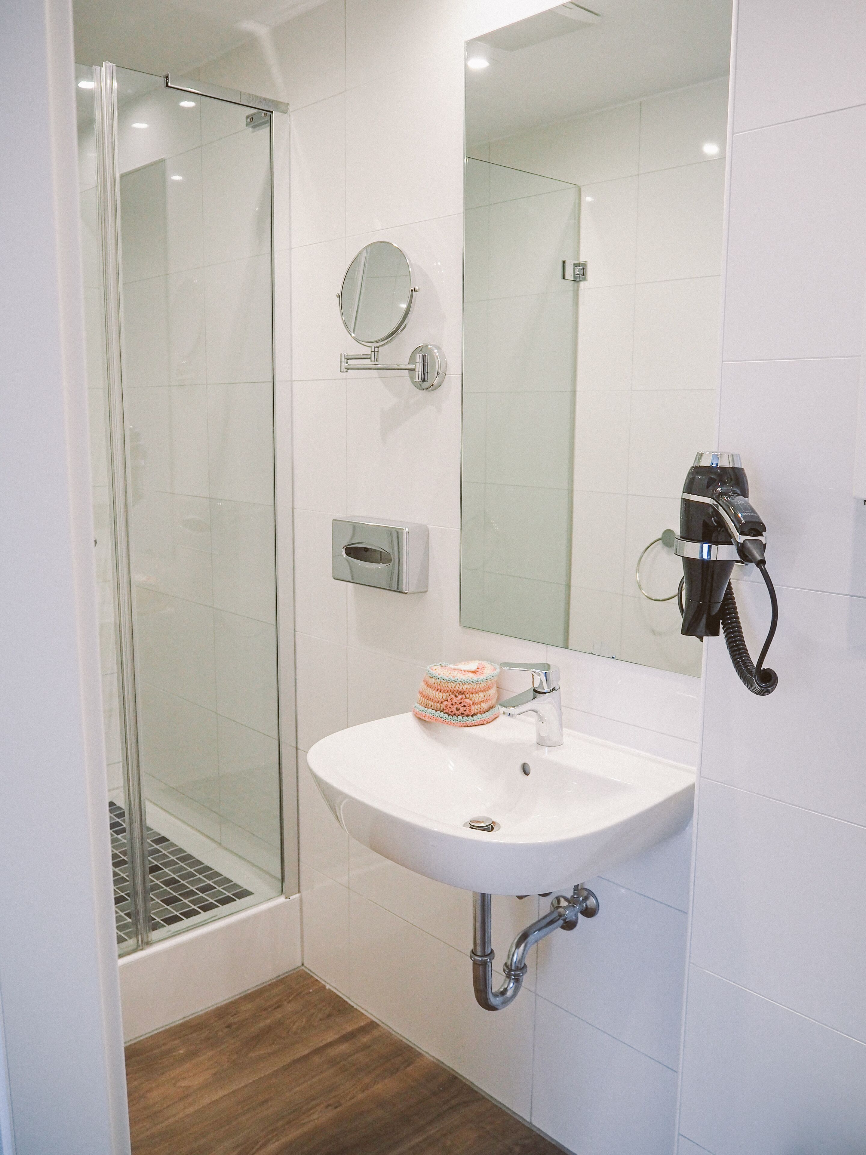 Un baño moderno con cabina de ducha de vidrio, un lavamanos blanco con espejo y un perchero.