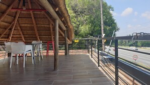 A covered outdoor seating area with a thatched roof, a tiled floor, and a view of a road with a speed limit sign. - FM GUEST LODGE (Randburg)