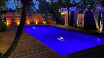 A swimming pool with a wooden deck and palm trees.