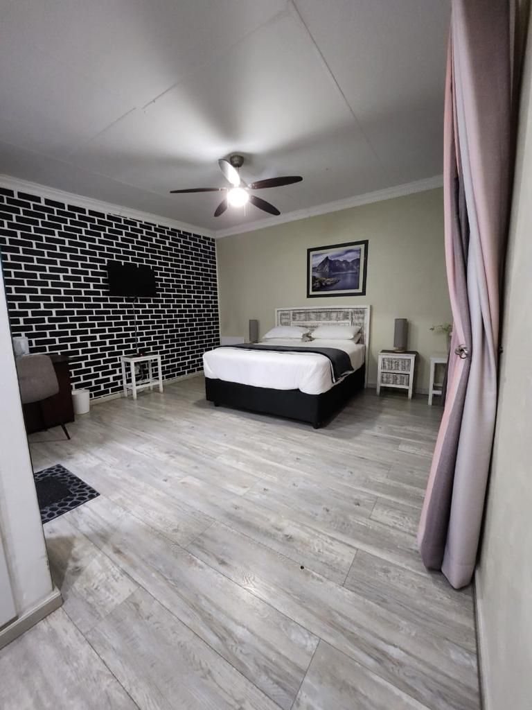 Une chambre à coucher avec un lit, un ventilateur de plafond, un mur décoré d’un motif en briques, un téléviseur fixé au mur et un tableau encadré accroché au mur.