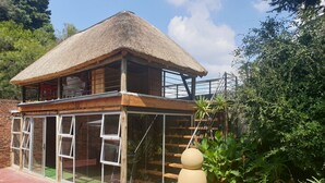 A house with a thatched roof, large windows, and a wooden deck. - FM GUEST LODGE (Randburg)