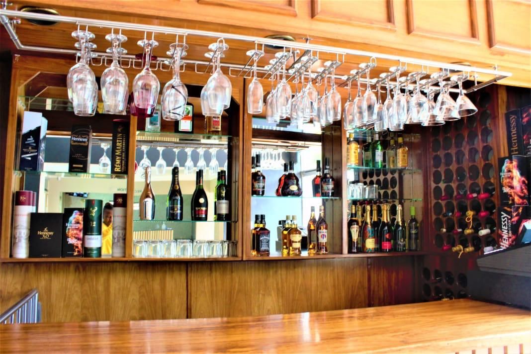 A bar area with hanging wine glasses, shelves of liquor bottles, and a wooden counter.