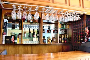 Een bar met hangende wijn glazen, drankflessen op planken en een houten toonbank.