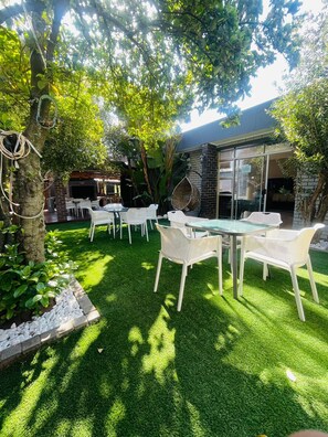 An outdoor seating area with tables and chairs, surrounded by lush greenery and trees.