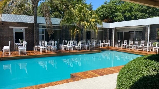 A swimming pool with white chairs and a wooden deck. - FM GUEST LODGE (Randburg)