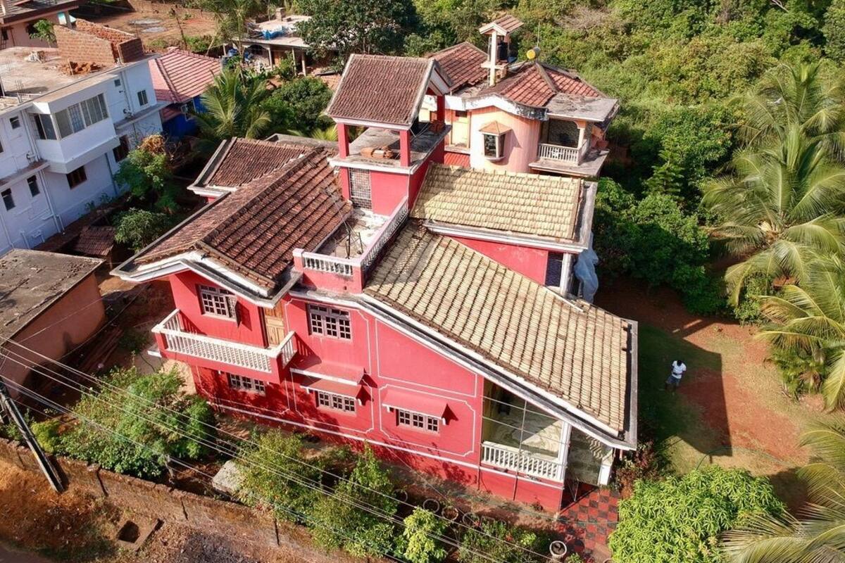 A multi-story building with a red facade and tiled roof, surrounded by greenery and other structures.