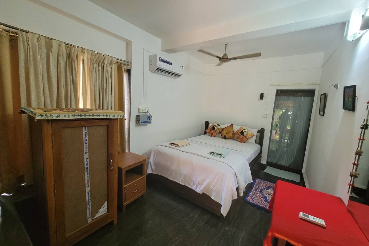 A bedroom with a bed, a wardrobe, a ceiling fan, and an air conditioning unit.