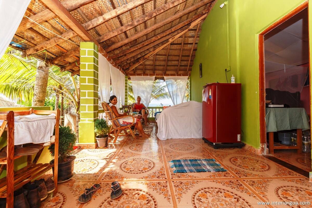 A room with a tiled floor, a bed, a red refrigerator, and a table with a checkered tablecloth.