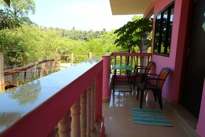 A balcony with a table and chairs, a view of greenery, and a pink wall.
