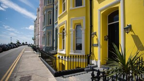 Une rangée de bâtiments aux couleurs vives, avec une façade jaune, une clôture en fer noir et un ciel dégagé.