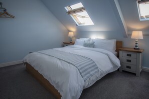 Ein Schlafzimmer mit Oberlicht, einem Bett mit weißer Bettwäsche, zwei Nachttischen mit Lampen und einem Holz-Kopfteil.
