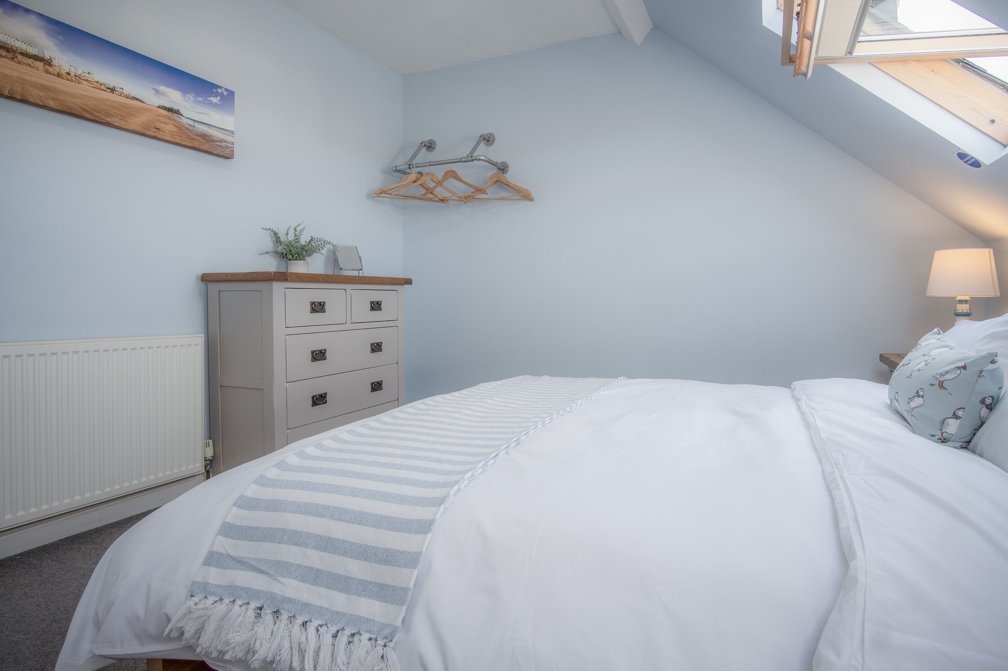 A bedroom with a bed, a dresser, a radiator, a wall-mounted coat rack, and a skylight.