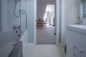 Ein Badezimmer mit Badewanne, Dusche und Waschbecken. Eine Tür führt zu einem Essbereich mit Tisch und Stühlen.