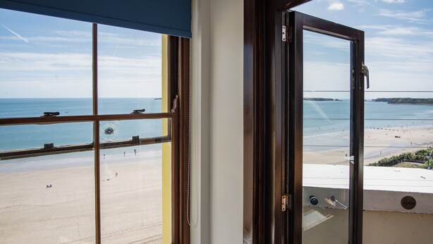 Une vue depuis un balcon donnant sur une plage, avec un ciel dégagé.