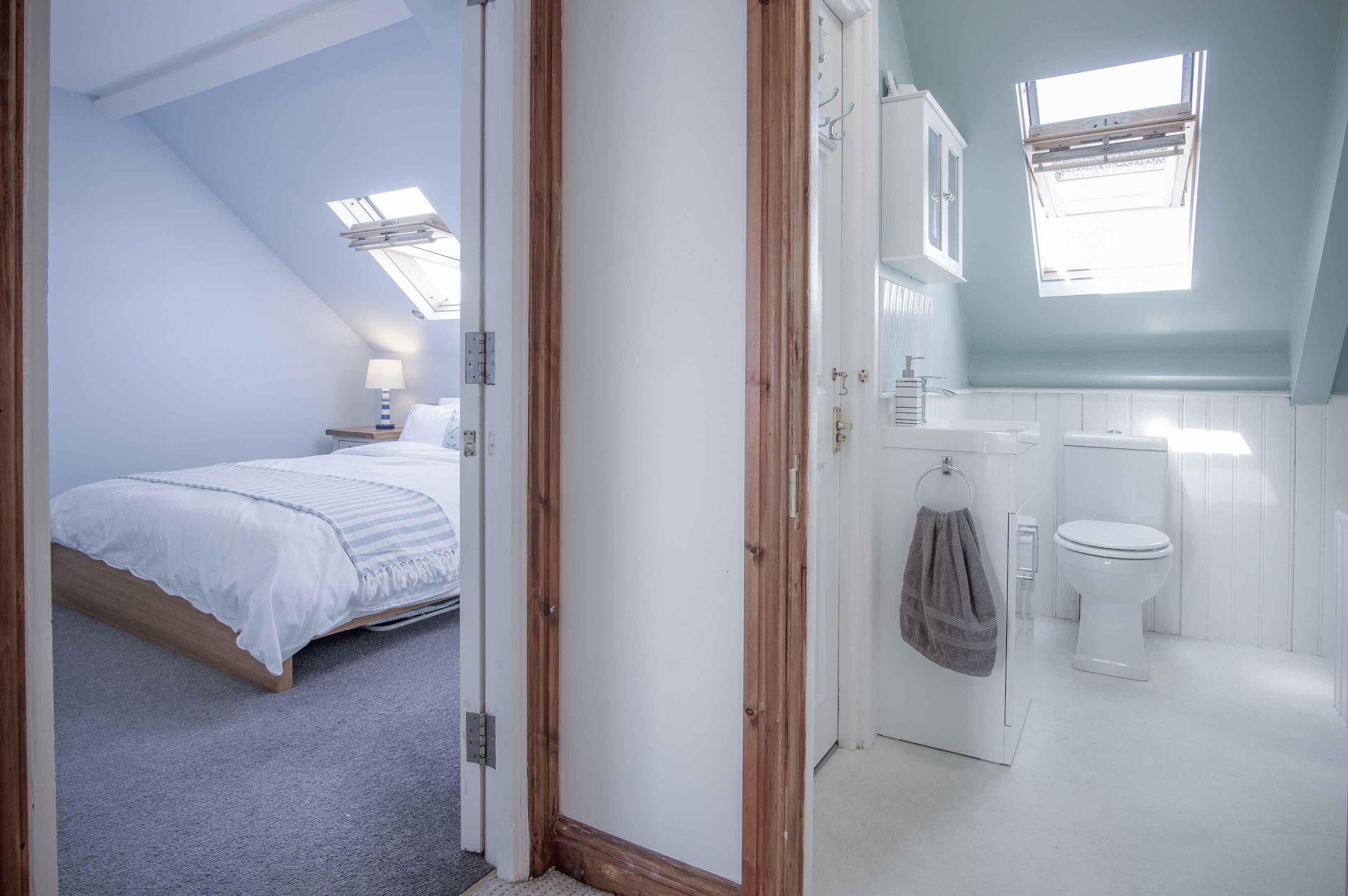 A bedroom with a bed, a nightstand, and a window. The bathroom has a toilet, a sink, and a window.