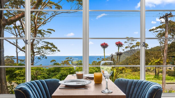 A dining table with two chairs, a candle, a glass of juice, and a glass of water. - Romantic Ocean View Studio @ Stanwell Tops (Stanwell Tops)