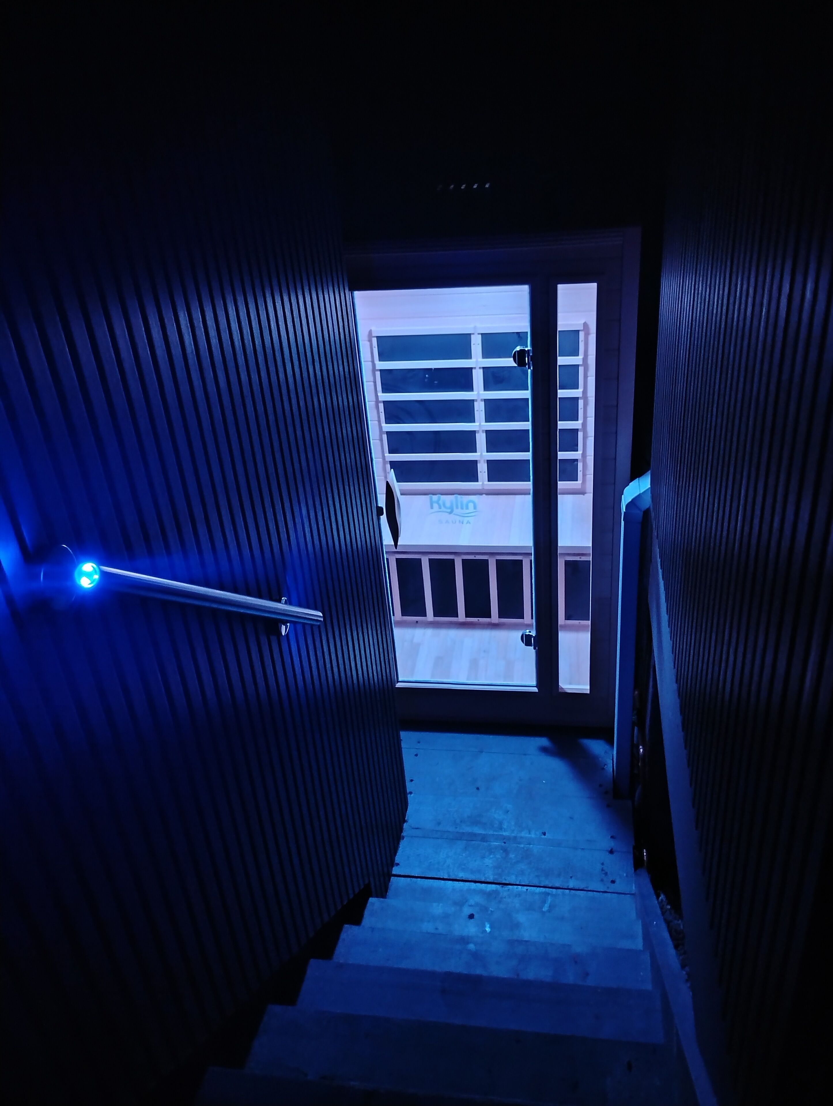 A hallway with a blue-lit handrail, a door leading to a room with a window, and a sign reading 'Kylin Sauna'.