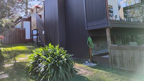 A modern building with vertical siding, a covered outdoor area, and a garden with a large plant. - Romantic Ocean View Studio @ Stanwell Tops (Stanwell Tops)
