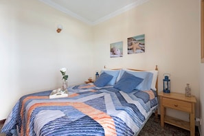 A bedroom with a bed, a nightstand, a vase with flowers, and two wall-mounted pictures.