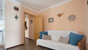 A living room with a white sofa, blue pillows, a wooden door, and wall decorations including a ship's wheel and a framed picture. - Vacation Home 'Marazul' with Sea View, Balcony & Wi-Fi (Tacoronte)