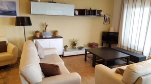 Un salon comprenant un canapé, une table basse, un téléviseur et un meuble contenant des objets décoratifs.