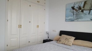 Ein Schlafzimmer mit einem Bett, einem Nachttisch, einer Lampe, einem Kleiderschrank und einem Gemälde eines Schiffes an der Wand.