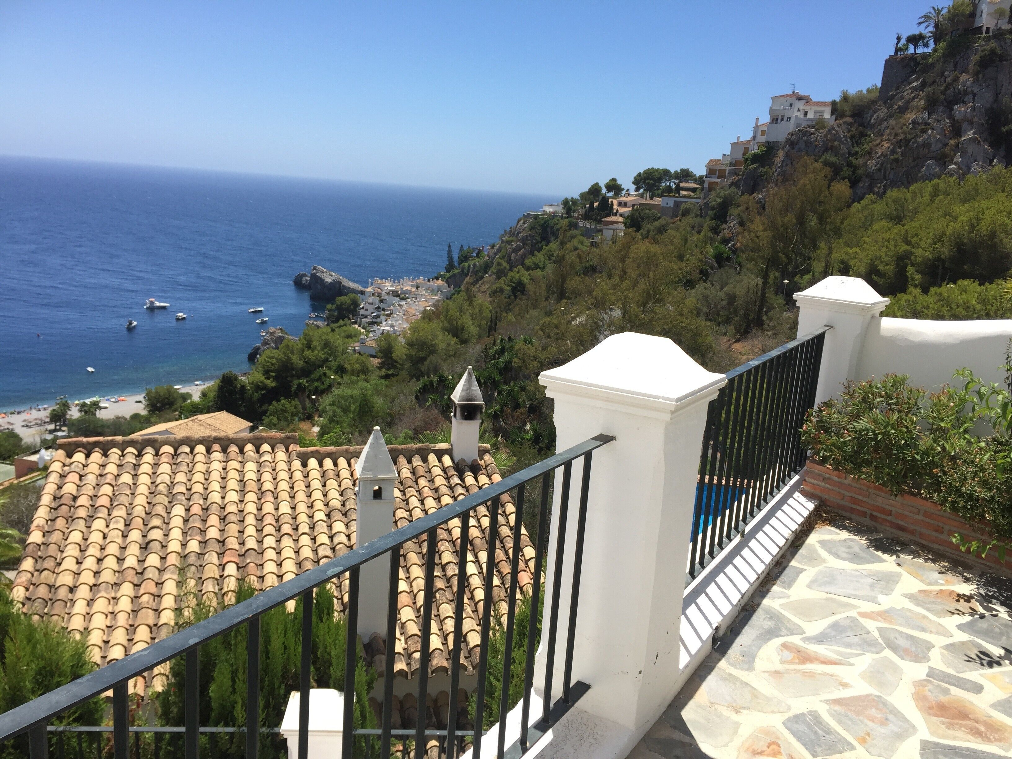 A coastal view with a tiled roof, a white building with a bell tower, and a stone pathway.